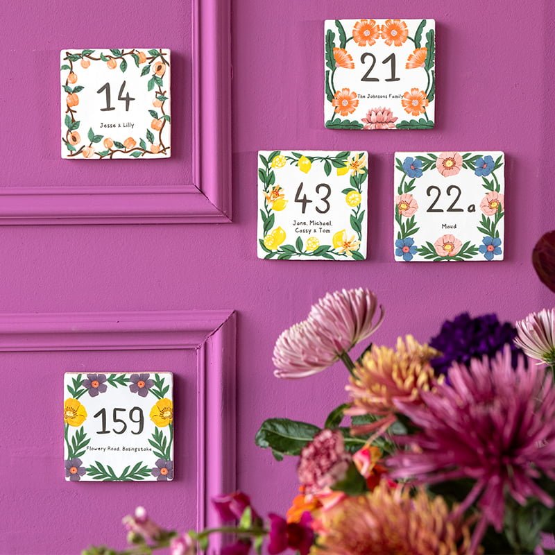 Huisnummer tegeltjes met kleurrijke bloemen op paarse muur achtergrond