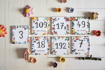 Tegeltjes met huisnummers omringd door kleurrijke bloemen op tafel