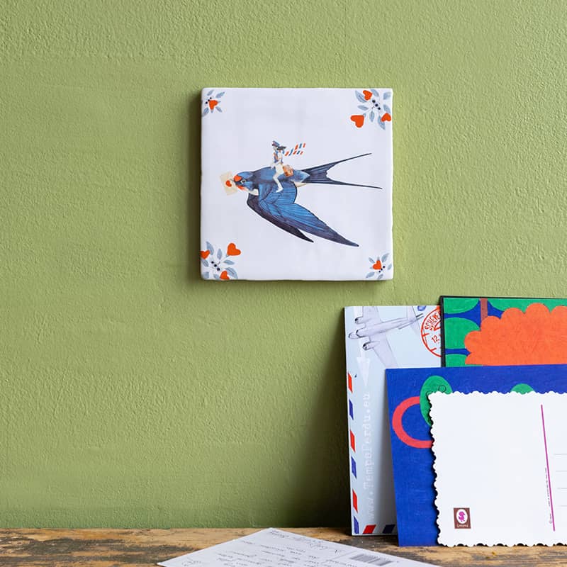 StoryTiles tegeltje met blauwe vogel met envelopje in zijn snavel op groene muur