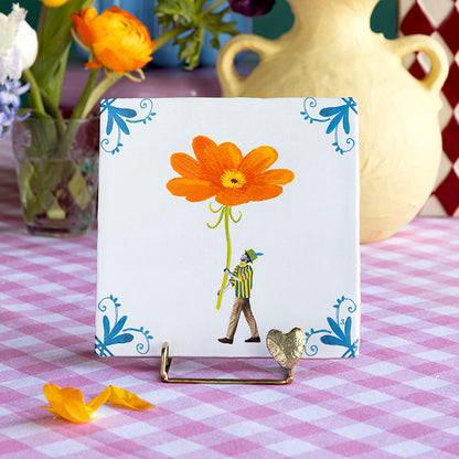 Figuurtje met hoed op de tegel Bringing you a bloom draagt grote rode bloem