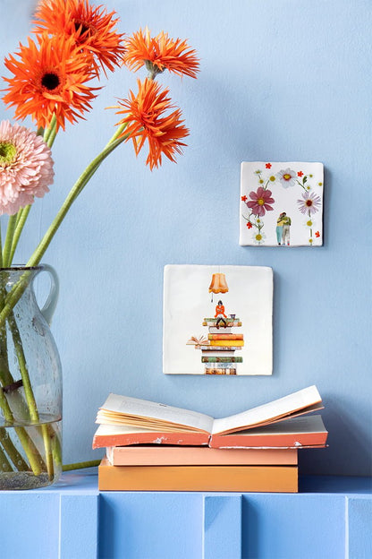 Tegeltjes met bloemen en figuurtje dat leest op blauwe muur