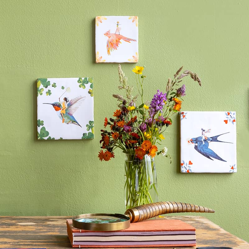 Kleurrijke tegeltjes met vogels aan groene muur naast boeket
