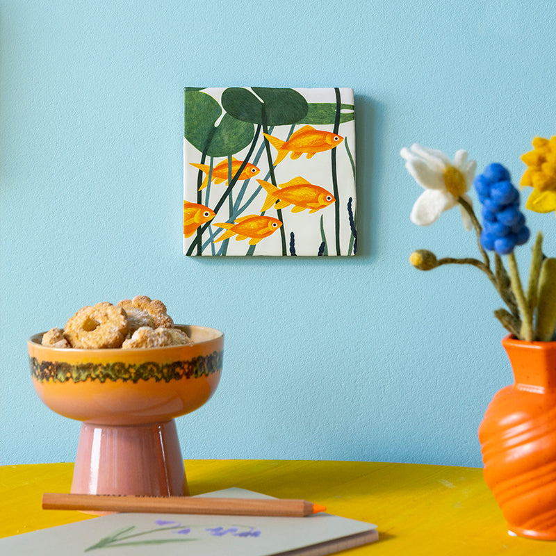 tegeltje met groep oranje goudvissen opgehangen op een lichtblauwe wand